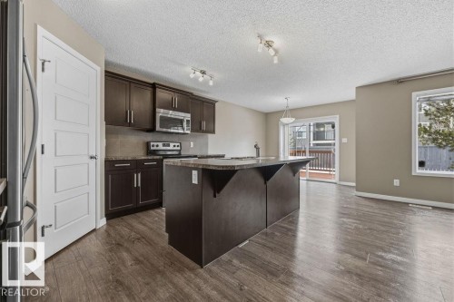 This kitchen features dark wood cabinetry, stainless steel appliances, and a central island with a granite countertop - 7873 170A Avenue, Edmonton, AB - Indoor Photo Showing Kitchen With Upgraded Kitchen