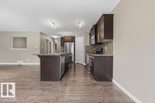 Spacious open-concept kitchen featuring dark wood cabinetry, granite countertops, stainless steel appliances, and a large central island - 7873 170A Avenue, Edmonton, AB - Indoor Photo Showing Kitchen