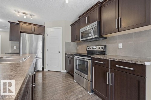 The kitchen features dark wood cabinetry, stainless steel appliances, and a double basin sink - 7873 170A Avenue, Edmonton, AB - Indoor Photo Showing Kitchen With Stainless Steel Kitchen With Double Sink With Upgraded Kitchen