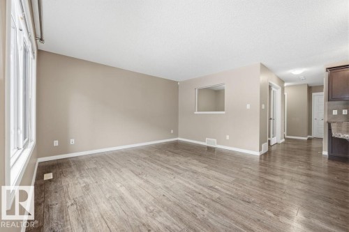 This spacious living area features wood-look flooring, light-colored walls, and windows providing natural light - 7873 170A Avenue, Edmonton, AB - Indoor Photo Showing Other Room