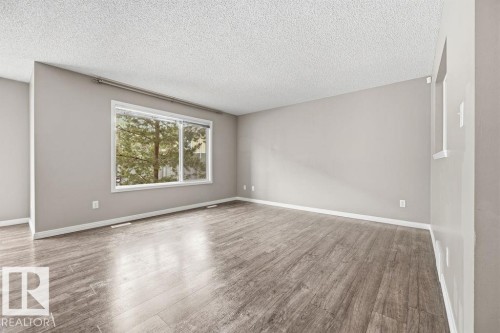 Spacious room featuring light-toned walls, wood-look flooring, and a large window providing views of greenery - 7873 170A Avenue, Edmonton, AB - Indoor Photo Showing Other Room