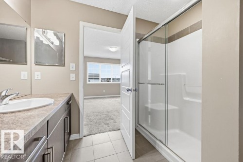 The bathroom features a vanity with a countertop and undermount sink, a shower with a sliding glass door, and tiled flooring - 7873 170A Avenue, Edmonton, AB - Indoor Photo Showing Bathroom