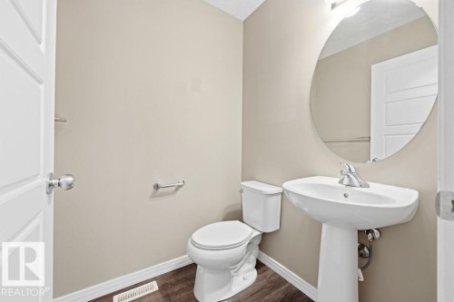 This powder room features a pedestal sink with a chrome faucet, a white toilet, and an oval mirror - 7873 170A Avenue, Edmonton, AB - Indoor Photo Showing Bathroom