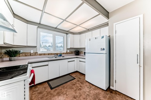 The kitchen features white cabinetry, a corner window above the sink, and a tiled backsplash - 7512 136 Avenue, Edmonton, AB - Indoor Photo Showing Kitchen With Double Sink