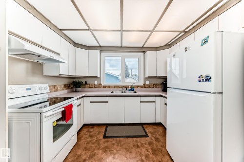 The kitchen features white cabinetry, a white refrigerator, a white electric range, and a window above the sink - 7512 136 Avenue, Edmonton, AB - Indoor Photo Showing Kitchen With Double Sink