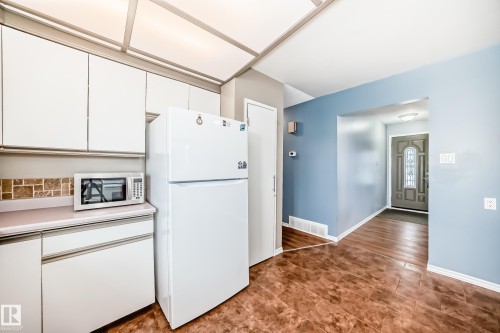 The property features white kitchen cabinetry, a tiled backsplash, and a white refrigerator - 7512 136 Avenue, Edmonton, AB - Indoor Photo Showing Kitchen