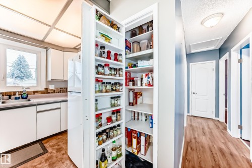 The kitchen features white cabinetry, a window with an exterior view, and a built-in pantry with shelving - 7512 136 Avenue, Edmonton, AB - Indoor