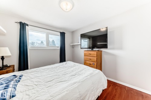 This room features hardwood floors, light-colored walls, and a window with dark curtains - 7512 136 Avenue, Edmonton, AB - Indoor Photo Showing Bedroom