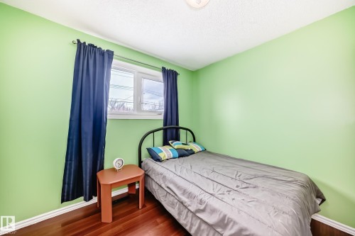 This room features hardwood flooring, light green walls, a window with blue curtains, and a ceiling light fixture - 7512 136 Avenue, Edmonton, AB - Indoor Photo Showing Bedroom