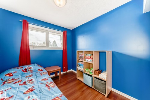 This room features hardwood flooring, blue painted walls, and a window with red curtains - 7512 136 Avenue, Edmonton, AB - Indoor Photo Showing Bedroom