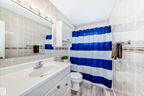 Bathroom featuring tiled walls, a vanity with an integrated sink, and a shower with a blue and white striped curtain - 7512 136 Avenue, Edmonton, AB - Indoor Photo Showing Bathroom