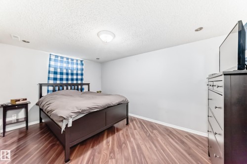 This room features hardwood flooring, white walls, and a window with blue and white checked curtains - 7512 136 Avenue, Edmonton, AB - Indoor Photo Showing Bedroom