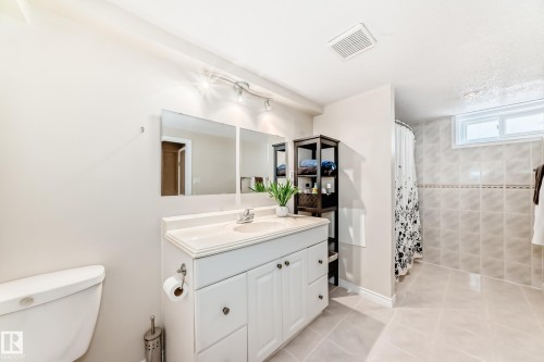 Bathroom featuring a white vanity with a single sink, a toilet, a shower area with tiled walls, and a window - 7512 136 Avenue, Edmonton, AB - Indoor Photo Showing Bathroom