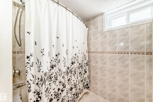 Bathroom featuring tiled walls, a shower with a flexible hose, and a window for natural light - 7512 136 Avenue, Edmonton, AB - Indoor Photo Showing Bathroom