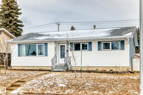 The property features white siding with blue shutters, a front door with a decorative screen, and a covered front entry with railings - 7512 136 Avenue, Edmonton, AB - Outdoor