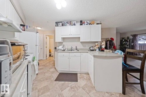The kitchen features white cabinetry, a light-colored countertop, and a patterned floor - 103 12110 119 Ave, Edmonton, AB - Indoor Photo Showing Kitchen With Double Sink