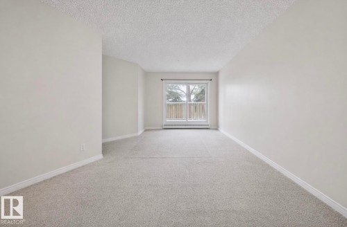 The room features light gray carpeting, white walls, and a window with white trim - 103 12110 119 Ave, Edmonton, AB - Indoor Photo Showing Other Room