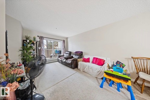 The living area features light-colored carpeting, a sliding glass door leading to an outdoor space, and white walls - 103 12110 119 Ave, Edmonton, AB - Indoor