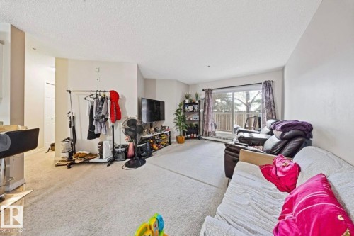 Living area featuring light-colored carpeting, light-toned walls, and a sliding glass door leading to a balcony - 103 12110 119 Ave, Edmonton, AB - Indoor