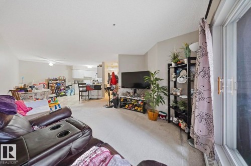 The open concept living area features light-colored carpeting, white walls, and a ceiling fan - 103 12110 119 Ave, Edmonton, AB - Indoor