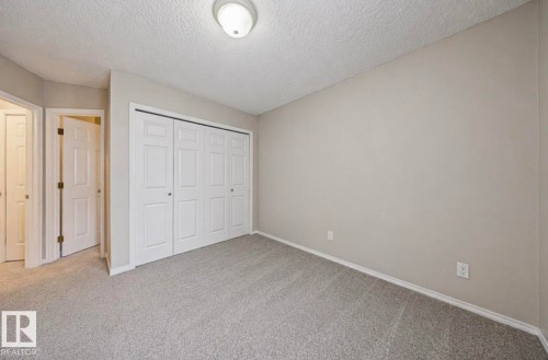 This room features neutral-toned walls, textured carpeting, and a built-in closet with bi-fold doors - 103 12110 119 Ave, Edmonton, AB - Indoor
