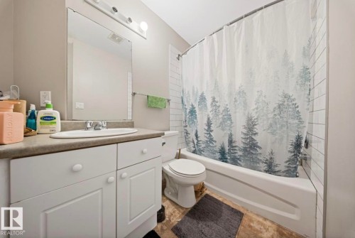 The bathroom features a vanity with a countertop and sink, a mirror, and a bathtub with a shower and white subway tile surround - 103 12110 119 Ave, Edmonton, AB - Indoor Photo Showing Bathroom