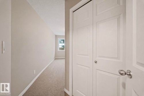 This interior space features light-colored walls and carpeting, with a window providing natural light at the far end - 103 12110 119 Ave, Edmonton, AB - Indoor Photo Showing Other Room