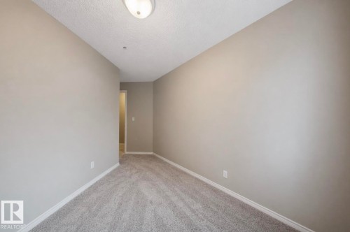 This room features light grey carpeting, light grey walls, white baseboards, and a ceiling-mounted light fixture - 103 12110 119 Ave, Edmonton, AB - Indoor Photo Showing Other Room