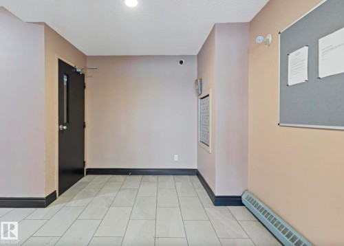 The property features light-colored tile flooring, dark trim, and a built-in wall unit - 103 12110 119 Ave, Edmonton, AB - Indoor Photo Showing Other Room