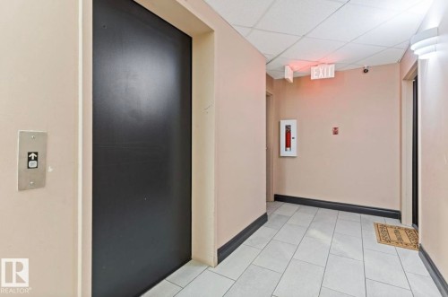 The property features an elevator with a call button, a hallway with light-colored walls, and a tiled floor - 103 12110 119 Ave, Edmonton, AB - Indoor Photo Showing Other Room