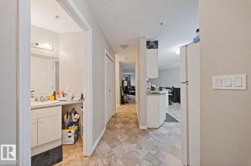 This interior hallway features neutral-toned walls, a light-colored tiled floor, and a white refrigerator - 103 12110 119 Ave, Edmonton, AB - Indoor Photo Showing Bathroom
