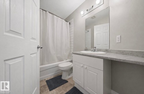 Bathroom featuring a white vanity with an integrated sink, a large mirror, and a combination shower and bathtub with a subway tile surround - 103 12110 119 Ave, Edmonton, AB - Indoor Photo Showing Bathroom