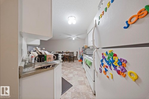 The kitchen features white cabinetry and white appliances, including a refrigerator and stove - 103 12110 119 Ave, Edmonton, AB - Indoor Photo Showing Other Room