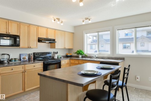 The kitchen features light wood cabinetry, a black oven and microwave, and track lighting - 67 12050 17 Avenue, Edmonton, AB - Indoor Photo Showing Kitchen