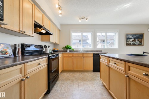 The kitchen features light wood cabinetry, dark countertops, and black appliances - 67 12050 17 Avenue, Edmonton, AB - Indoor Photo Showing Kitchen With Double Sink