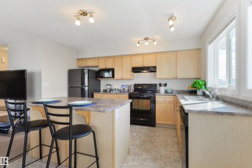 The kitchen features light wood cabinetry, dark countertops, and black appliances, including a range, refrigerator, and microwave - 67 12050 17 Avenue, Edmonton, AB - Indoor Photo Showing Kitchen