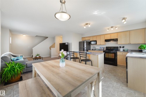 The property features a bright kitchen with light wood cabinetry, black appliances, and a central island with seating - 67 12050 17 Avenue, Edmonton, AB - Indoor