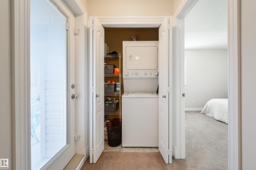 Convenient laundry area featuring a stacked washer and dryer, with shelving for storage, and carpeted flooring - 67 12050 17 Avenue, Edmonton, AB - Indoor Photo Showing Laundry Room