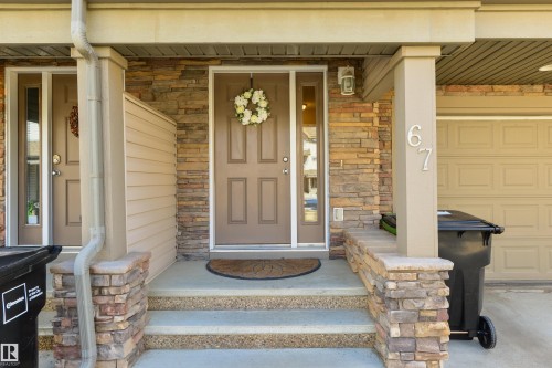 The property features a stone facade and a welcoming front entrance with a brown door and a light fixture - 67 12050 17 Avenue, Edmonton, AB - Outdoor With Exterior