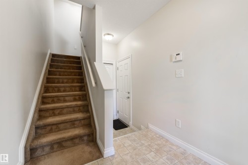 Entryway featuring a carpeted staircase with white risers and handrail, neutral painted walls, and tile flooring - 67 12050 17 Avenue, Edmonton, AB - Indoor Photo Showing Other Room