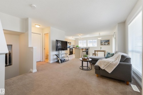 This property features an open-concept living area with neutral carpeting, recessed lighting, and large windows with blinds - 67 12050 17 Avenue, Edmonton, AB - Indoor Photo Showing Living Room