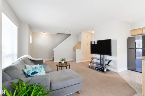 Living area featuring neutral-toned carpet, a staircase with white risers, and a window with blinds - 67 12050 17 Avenue, Edmonton, AB - Indoor