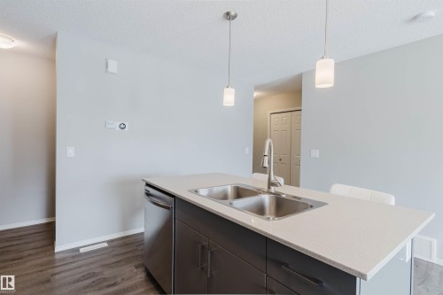 The kitchen features a functional island with a double stainless steel sink, a modern faucet, and a dishwasher - 17268 9B Avenue, Edmonton, AB 