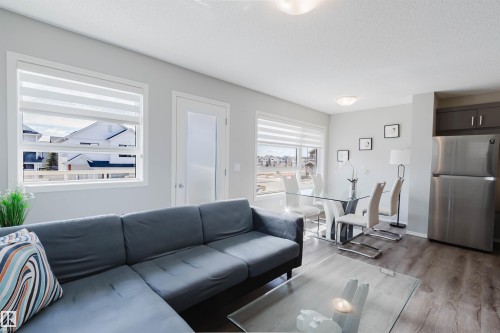 The open concept living area features large windows with blinds, light-colored walls, and wood-style flooring - 17268 9B Avenue, Edmonton, AB 
