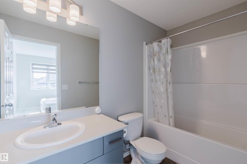 The bathroom features a white vanity with a rectangular sink and chrome faucet, a toilet, and a shower/tub combination with a shower curtain - 17268 9B Avenue, Edmonton, AB 
