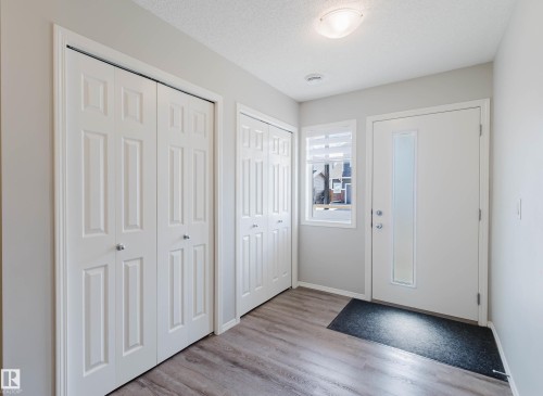 Entryway featuring wood-style flooring, a light-colored door with a frosted glass insert, and two panel-style closet doors - 17268 9B Avenue, Edmonton, AB 