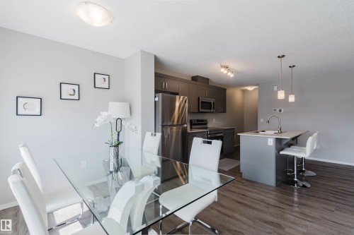 The open concept living area features a modern kitchen with stainless steel appliances, dark cabinetry, and a central island with bar seating - 17268 9B Avenue, Edmonton, AB 