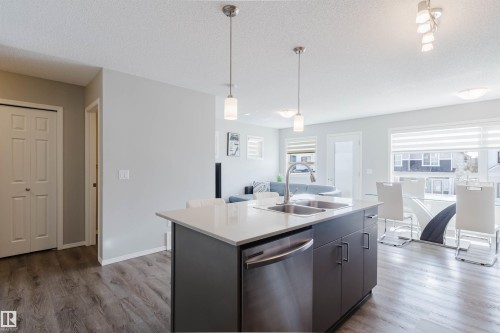 Well-appointed kitchen featuring an island with a stainless steel sink and dishwasher, pendant lighting, and light-colored countertops - 17268 9B Avenue, Edmonton, AB 