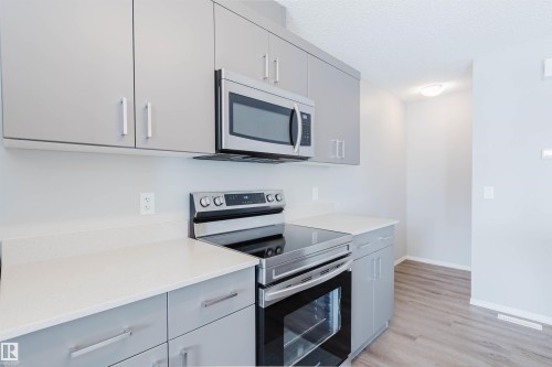 The kitchen features modern gray cabinetry, white countertops, and stainless steel appliances, including an oven, stove, and microwave - 17268 9B Avenue, Edmonton, AB 