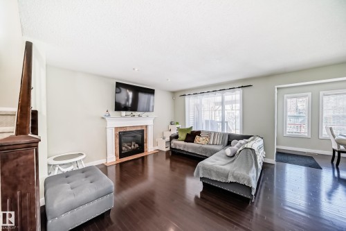 Living area featuring dark hardwood floors, a fireplace with a white mantel, recessed lighting, and windows providing natural light - 3433 Goodridge Link Link, Edmonton, AB - Indoor Photo Showing Living Room With Fireplace